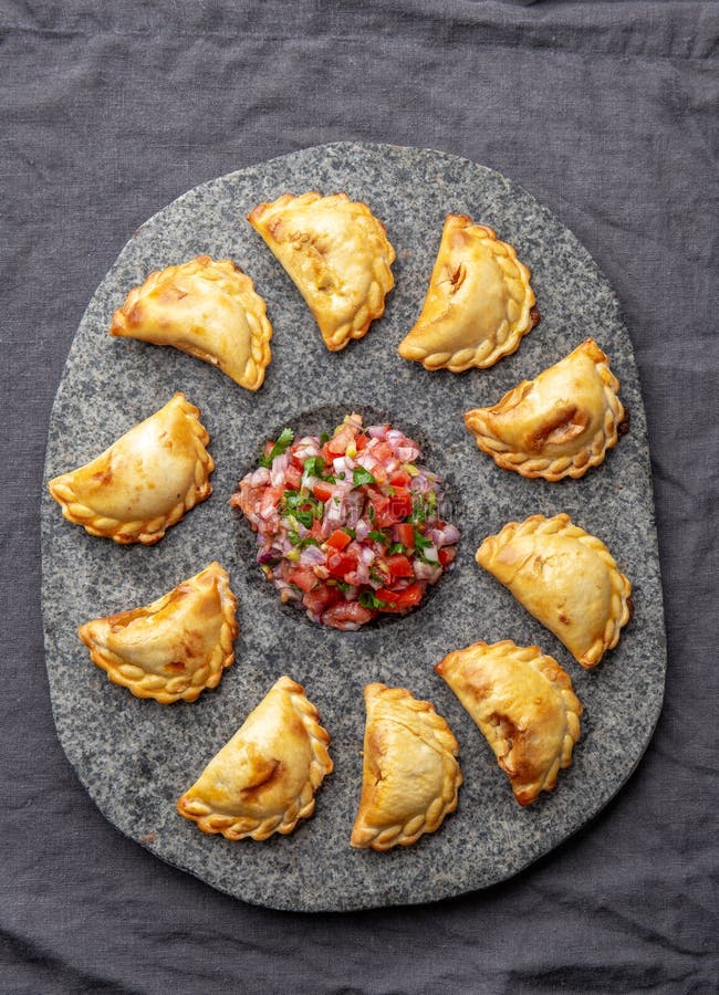 Different little cocktail EMPANADAS on stone plate with tomato sauce and guacamole . Gray background. Latin American and Spanish