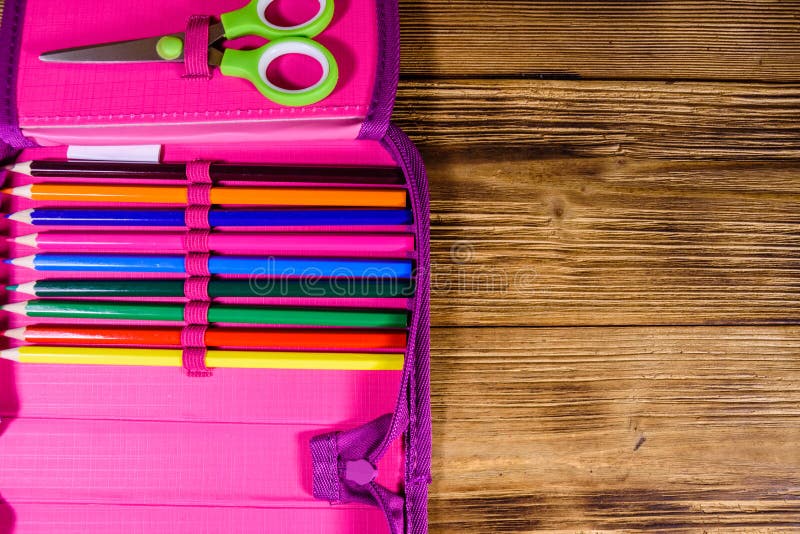 Different school stationeries pens, pencils and scissors in a pink pencil box. Top view