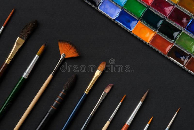 Different shape and size paintbrushes, set of watercolor paints on black paper sheet, top view, flat lay. Different shape and size paintbrushes, set of watercolor paints on black paper sheet, top view, flat lay