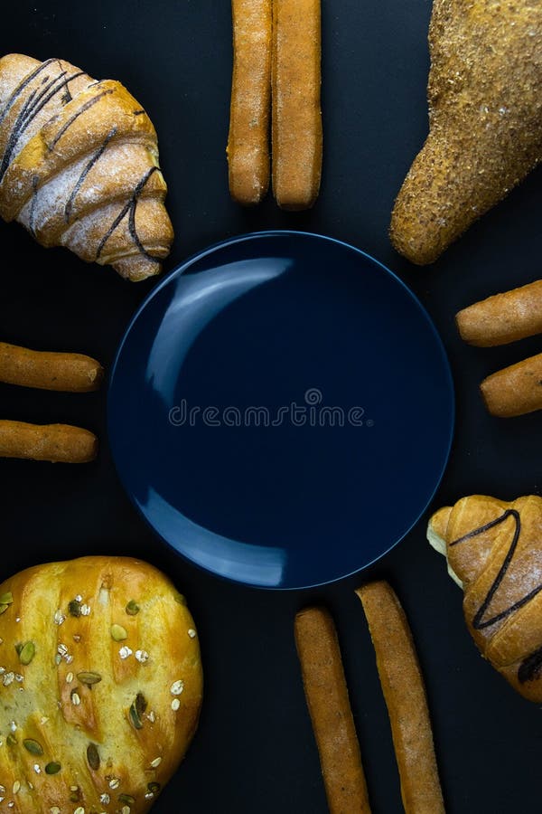 Different types of fresh bread with grain on a black rustic background. the bread stands around blue plate stock image