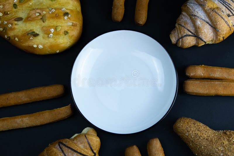 Different types of fresh bread with grain on a black rustic background. the bread stands around white plate stock photo