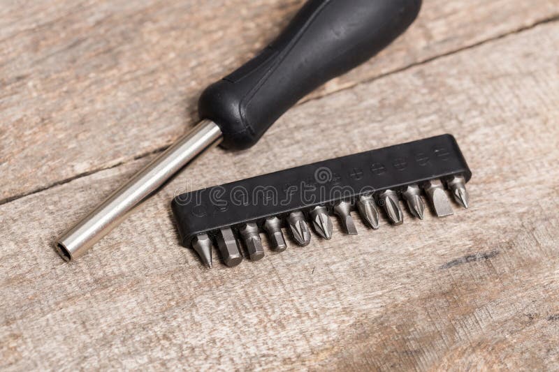 Different types of screwdriver bits placed next to a hand tool on a wooden surface stock photography