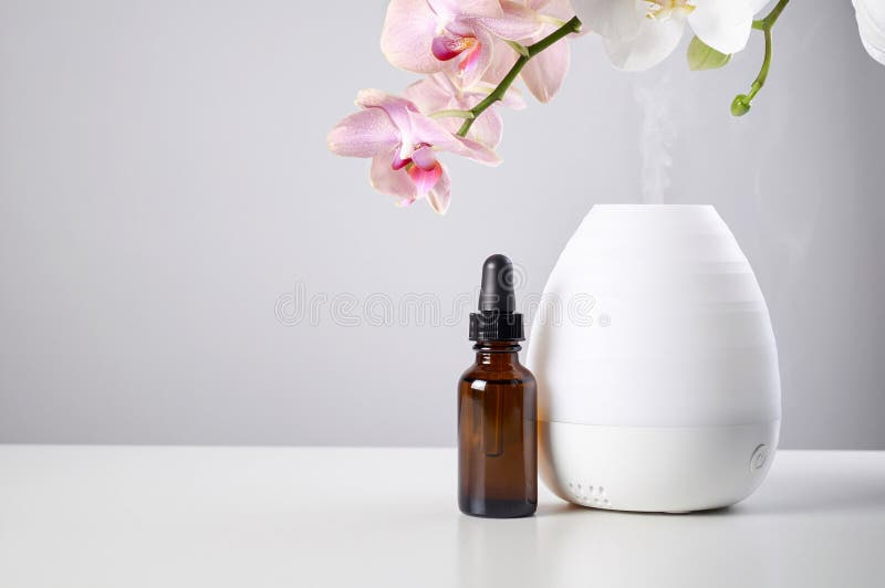 Diffuseur d'huile avec les fleurs ambres en verre de bouteille et d'orchidée sur la table blanche photos libres de droits Diffuseur d'huile avec les fleurs ambres en verre de bouteille et d'orchidée sur la table blanche photos libres de droits
