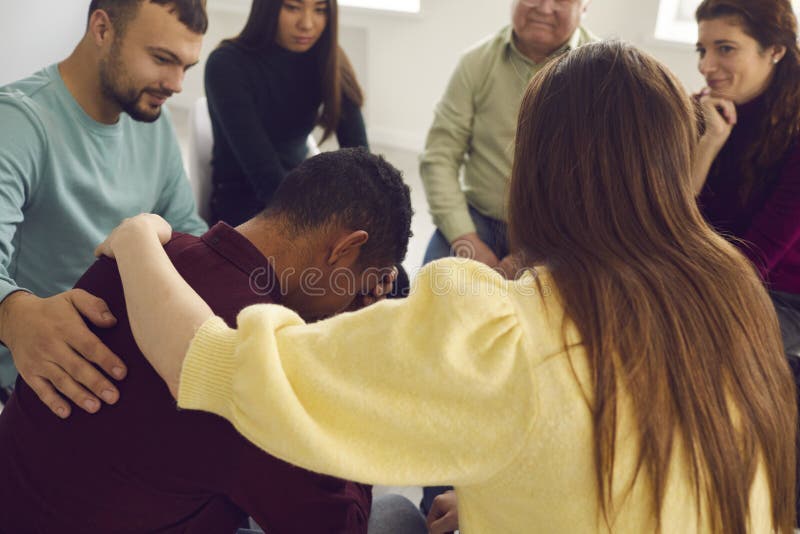 Friendly understanding people comforting young patient who& x27;s crying and telling his sad story in group therapy. Diverse friends supporting African-American men who& x27;s complaining about life problems. Friendly understanding people comforting young patient who& x27;s crying and telling his sad story in group therapy. Diverse friends supporting African-American men who& x27;s complaining about life problems