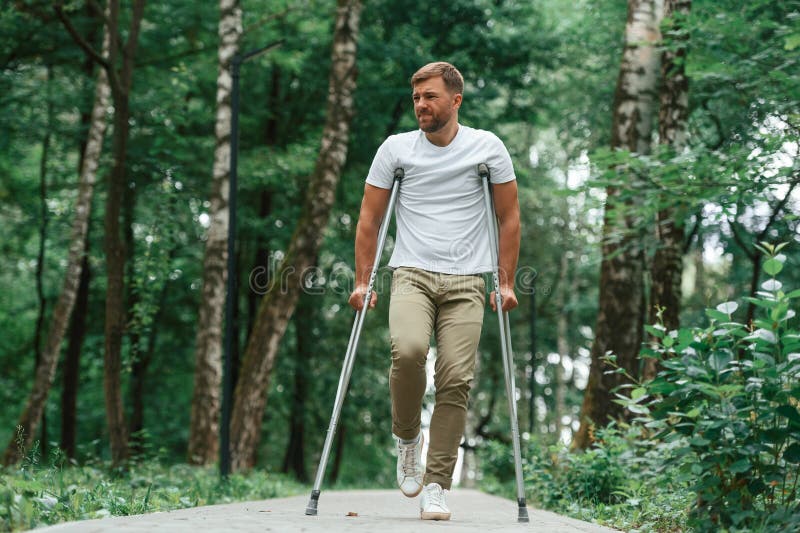 Difícil de caminar lucha para moverse por el dolor. hombre con muletas está en el parque al aire libre. lesión en la pierna fotografía de archivo
