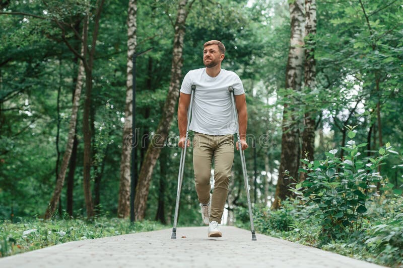 Difícil de caminar lucha para moverse por el dolor. hombre con muletas está en el parque al aire libre. lesión en la pierna foto de archivo libre de regalías
