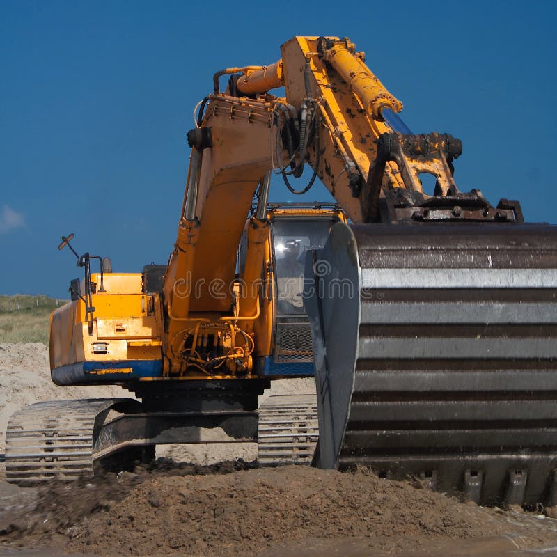 Action shot of an orange digger with its claw towards the camera moving earth.