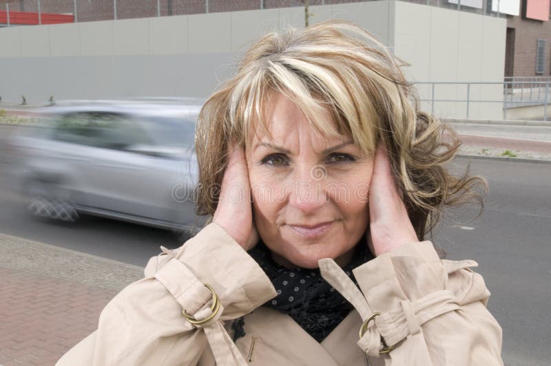 Mature woman with hands at the ears because of the loud noise of the street in the city. Mature woman with hands at the ears because of the loud noise of the street in the city.