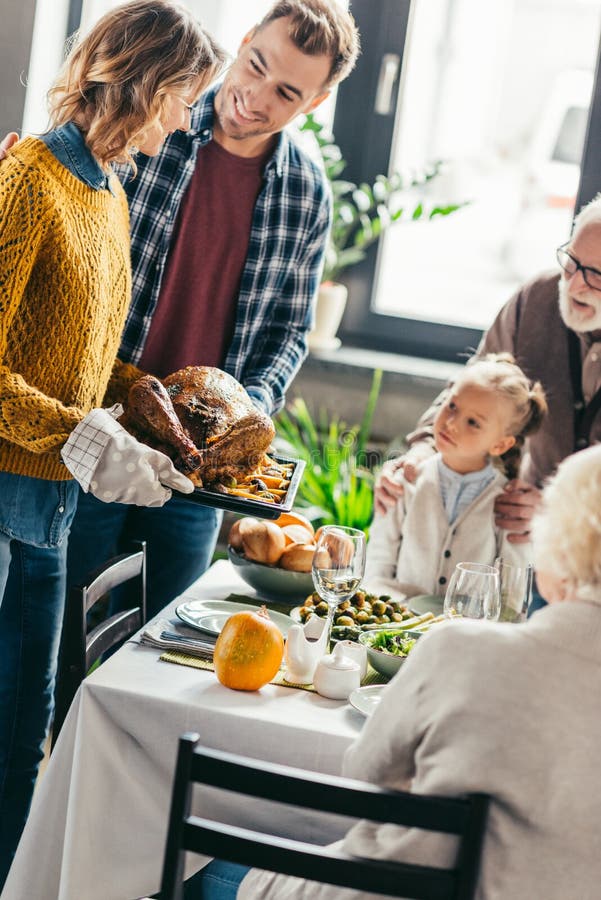 dinde de transport d'homme et de femme pour le dîner de thanksgiving tandis que regard enthousiaste de famille images stock dinde de transport d'homme et de femme pour le dîner de thanksgiving tandis que regard enthousiaste de famille images stock