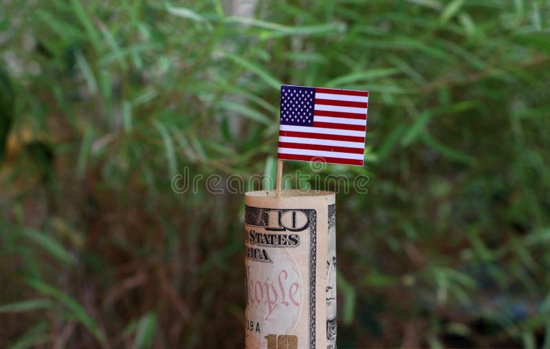 Dinero rodado del billete de banco diez d?lares americanos y palillos con la mini bandera de Am?rica en fondo verde de la natural imagen de archivo libre de regalías Dinero rodado del billete de banco diez d?lares americanos y palillos con la mini bandera de Am?rica en fondo verde de la natural imagen de archivo libre de regalías