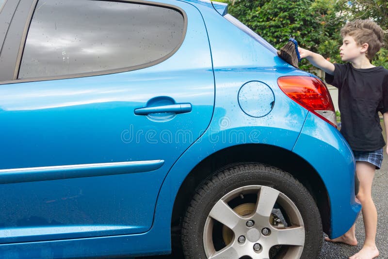 Dinero suelto de la ganancia del muchacho que limpia el coche compacto azul imagen de archivo