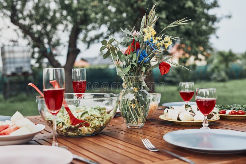 Dinner in an apple orchard on wooden table with salads and wine decorated with flowers