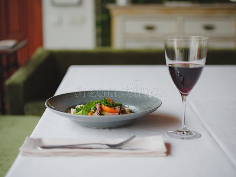 A dinner composition on a blurred restaurant background. A tasty dish next to a glass of red wine. Copy space.