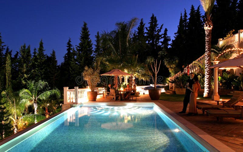 Fiesta sobre el El gran lujo espanol por la noche huéspedes charlando alrededor iluminado nadar piscina.