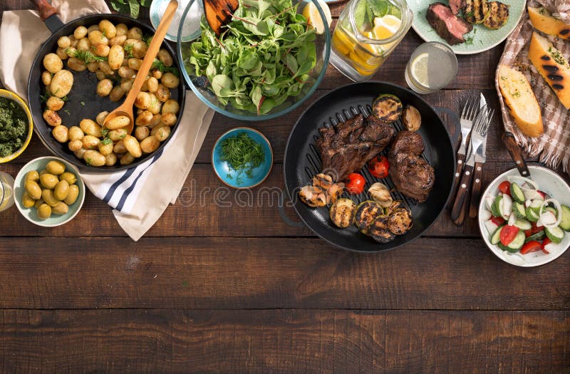 Dinner table with grilled steak, vegetables, potatoes, salad, sn