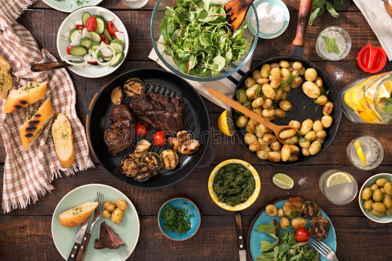 Dinner table with grilled steak, vegetables, potatoes, salad, sn