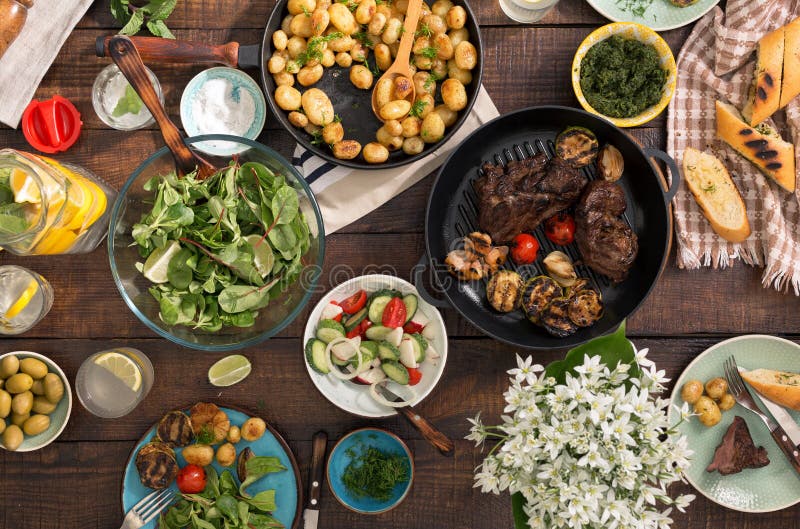 Dinner table with grilled steak, vegetables, potatoes, salad, sn