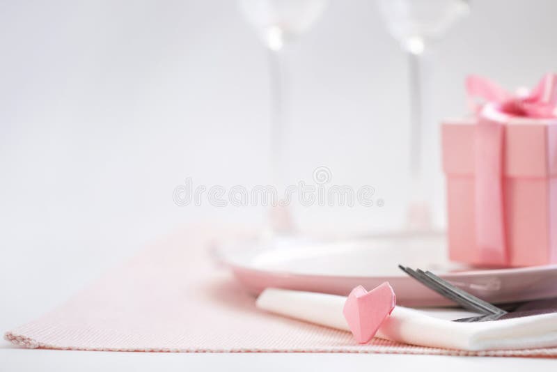 Dinner on Valentine`s day. Pink plate, Cutlery, pair of glasses, gift, heart on the table. stock photo Dinner on Valentine`s day. Pink plate, Cutlery, pair of glasses, gift, heart on the table. stock photo