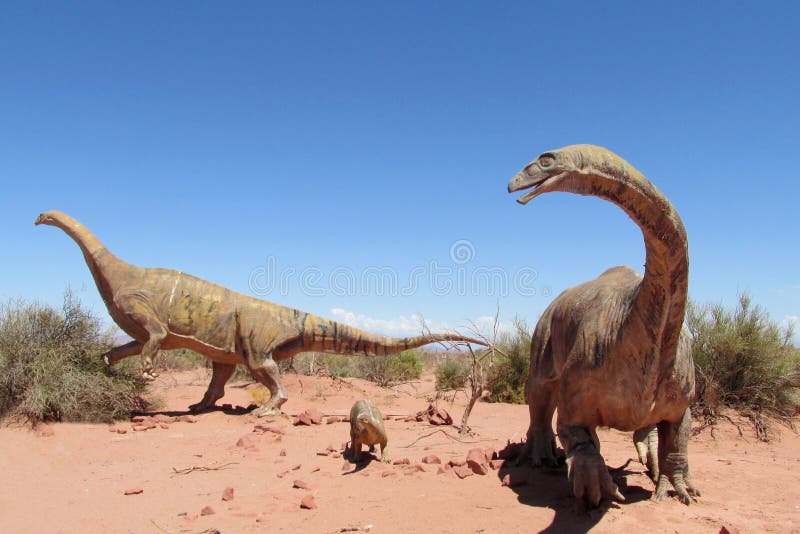 The statue, a model dinosaur standing on a red dry sand between the rocks. Artificial dinosaur. Jurassic Park. Models of dinosaurs in the museum, the National Park talampaya outdoors in Argentina. The statue, a model dinosaur standing on a red dry sand between the rocks. Artificial dinosaur. Jurassic Park. Models of dinosaurs in the museum, the National Park talampaya outdoors in Argentina.