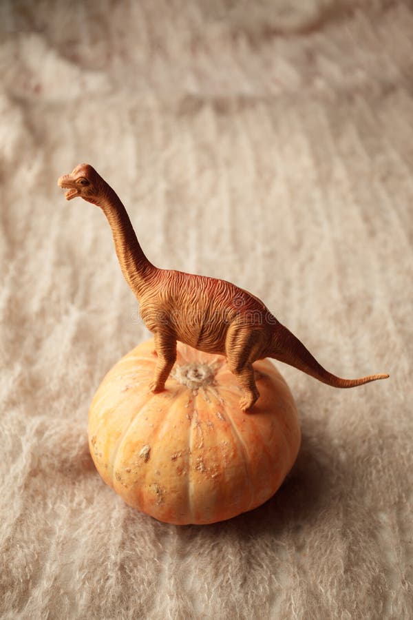 A dinosaur stands on a pumpkin on a brown background, a surreal concept, a monochrome. royalty free stock image A dinosaur stands on a pumpkin on a brown background, a surreal concept, a monochrome. royalty free stock image
