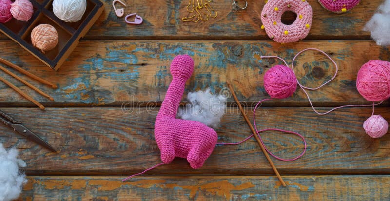 Crochet pink dinosaur. Making toy for child. On table threads, needles, hook, cotton yarn. Step 2. Stuff the toy with padding polyester. Handmade crafts. DIY concept. Income from hobby. Crochet pink dinosaur. Making toy for child. On table threads, needles, hook, cotton yarn. Step 2. Stuff the toy with padding polyester. Handmade crafts. DIY concept. Income from hobby