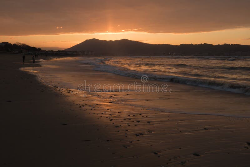 Direct golden sunset`s sunlight on a scenic sandy beach in hendaye in dramatic cloudy atmosphere, basque country, france. Direct golden sunset`s sunlight on a royalty free stock images Direct golden sunset`s sunlight on a scenic sandy beach in hendaye in dramatic cloudy atmosphere, basque country, france. Direct golden sunset`s sunlight on a royalty free stock images