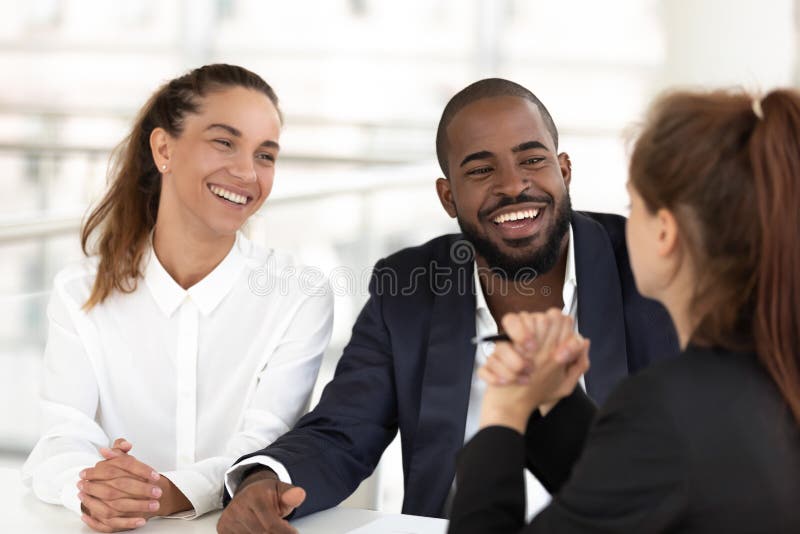 Multiracial businesspeople sitting at desk in modern office room, smiling diverse teammates enjoying talk to colleagues during teamwork or friendly hr managers interviewing vacancy candidature concept. Multiracial businesspeople sitting at desk in modern office room, smiling diverse teammates enjoying talk to colleagues during teamwork or friendly hr managers interviewing vacancy candidature concept