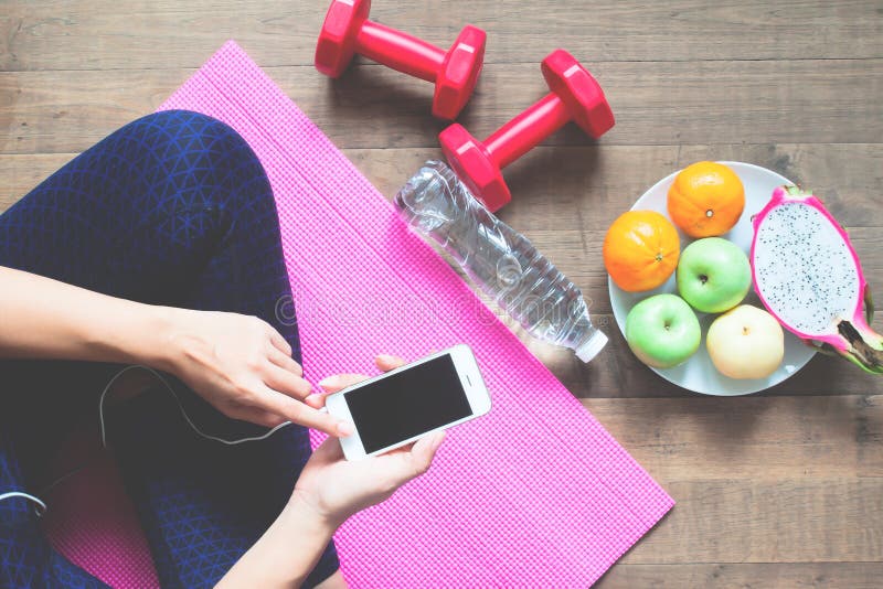 Directly above of woman in fitness clothing using mobile phone with sport equipments and fruits on the floor, Healthy royalty free stock photo Directly above of woman in fitness clothing using mobile phone with sport equipments and fruits on the floor, Healthy royalty free stock photo
