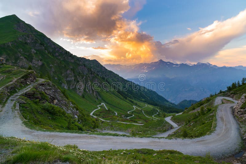 Dirt mountain road leading to high mountain pass in Italy Colle delle Finestre. Expasive view at sunset, colorful dramatic sky