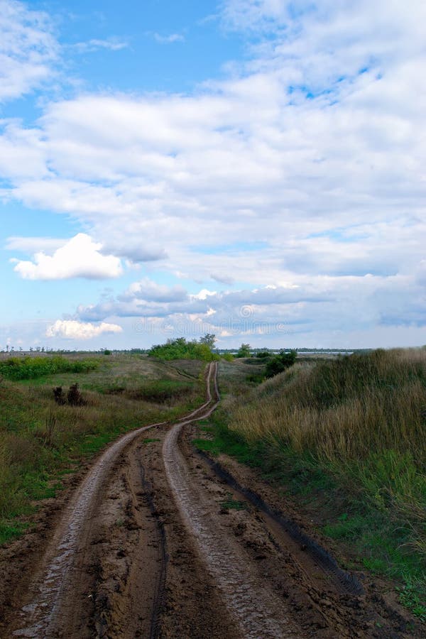 A Dirt Road Going Deep Into The Fields With Dense Clouds In The Sky