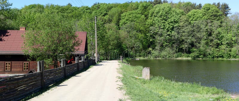 A dirt sandy road leads to the Lithuanian village along the shore of a clean lake