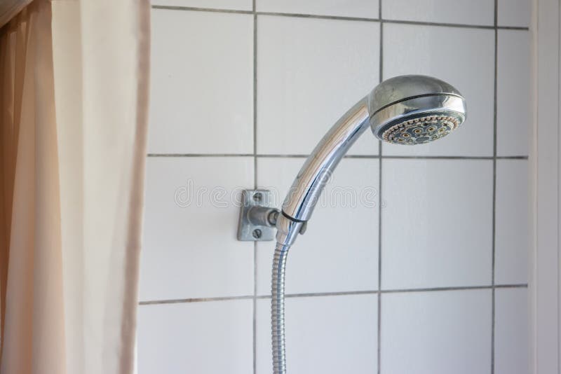 Dirty corroded limescale calcified shower head hanging from a stand inside cabin visible curtain stock photo