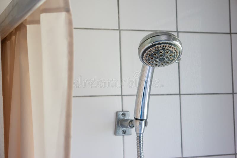 Dirty corroded limescale calcified shower head hanging from a stand inside cabin visible curtain stock image