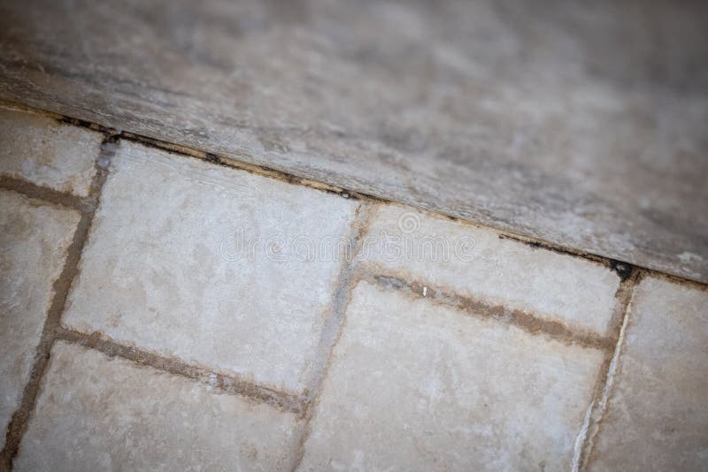 Dirty grout with beige tiles in a bathroom with mold, rust and soap residue.