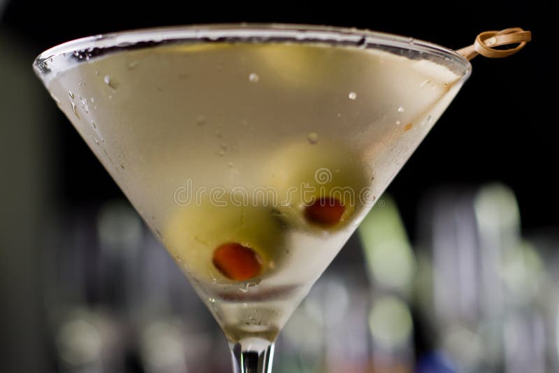 Dirty martini chilled and served on a busy bar top with a shallow depth of field and color lights and glasses in the background