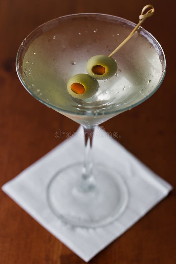 Dirty martini chilled and served on a busy bar top with a shallow depth of field and color lights and glasses in the background