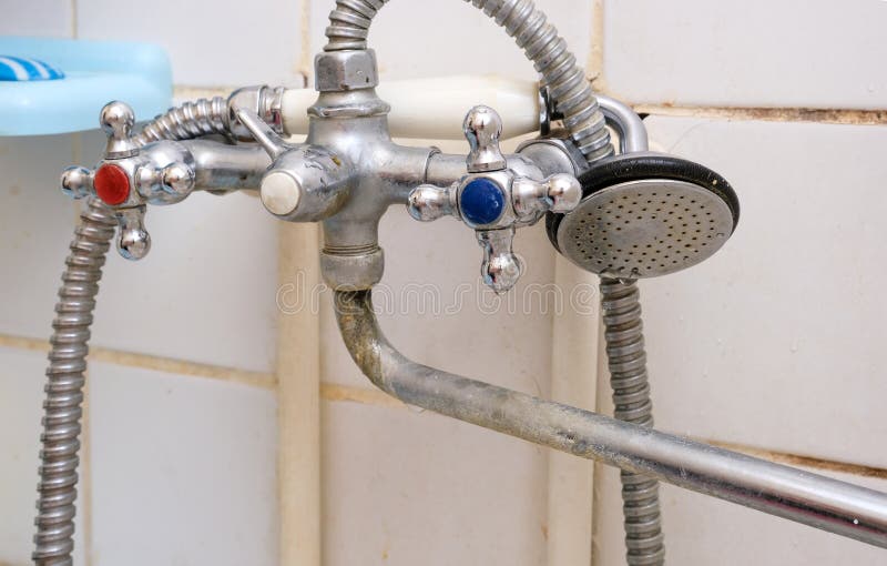 Dirty old faucet with limescale or lime scale on it, dirty calcified and rusty shower mixer tap and hose, moldy tiles on stock photography