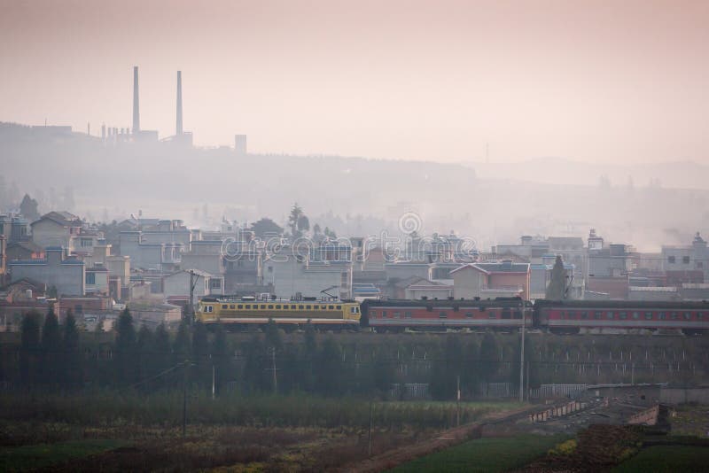 Dirty pollution. A train passes the old city of south Yunnan, China, land of coal. Coal mining with pipes on the mountain