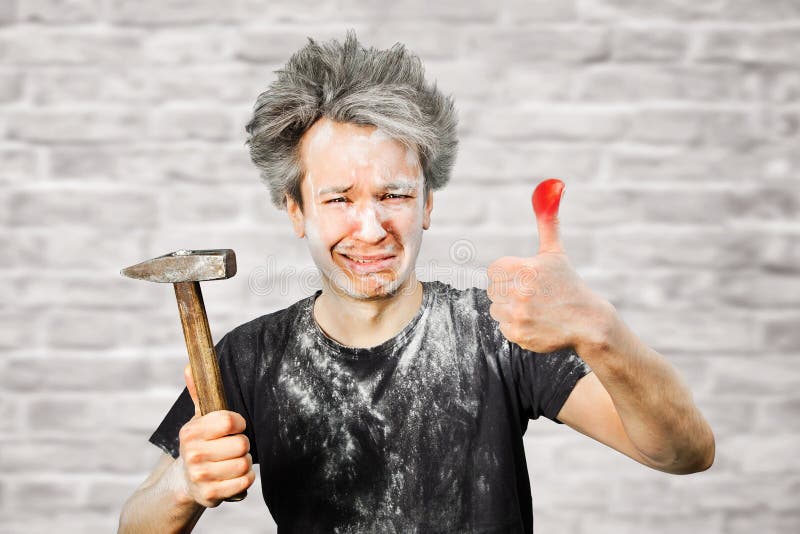 Dirty young builder guy fail is hold a hammer, hit the finger on brick wall background at home during repairs