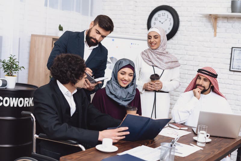 Disabled arab man in wheelchair working in office. Man is sharing notes with coworkers. royalty free stock photos Disabled arab man in wheelchair working in office. Man is sharing notes with coworkers. royalty free stock photos