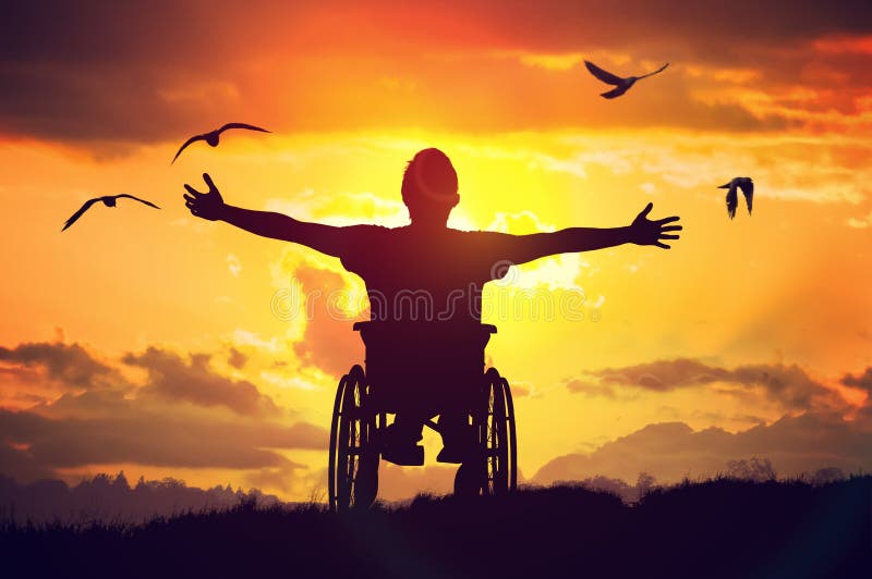 Disabled handicapped man has a hope. He is sitting on wheelchair and stretching hands at sunset