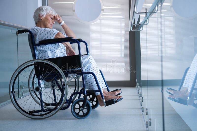 Disabled Senior Patient on Wheelchair in Hospital Passageway Stock