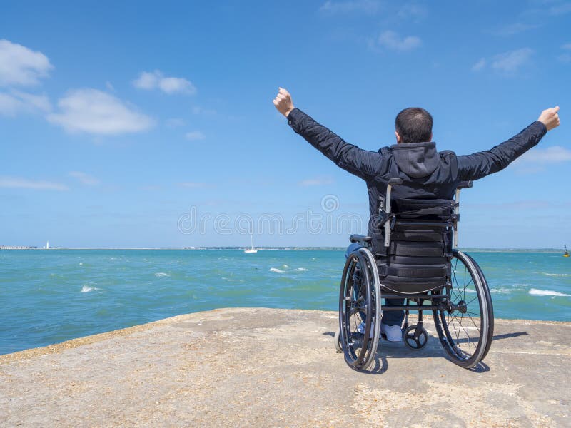 Disabled young man sitting in a wheelchair and looks at the sea