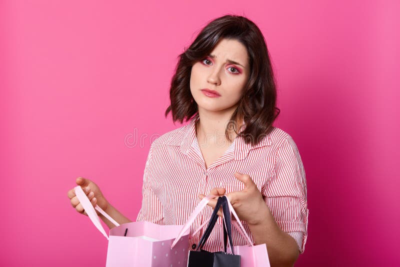 Disappointed dark haired woman, wears rose blouse, holds opened bag. Beautiful brunette looks unhappy, dislikes purchase. Bored royalty free stock photo Disappointed dark haired woman, wears rose blouse, holds opened bag. Beautiful brunette looks unhappy, dislikes purchase. Bored royalty free stock photo