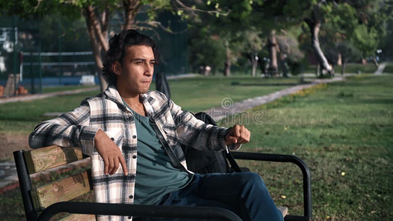 Disappointed lonely Latino guy waiting meeting checking time watch on bench at summer sunny park stock video footage