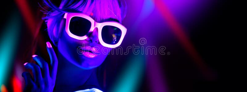Disco girl in neon light dancing in night club. Fashion model woman. Closeup portrait of beautiful girl with fluorescent make-up. Body Art design in UV. Sunglasses. Colorful make up