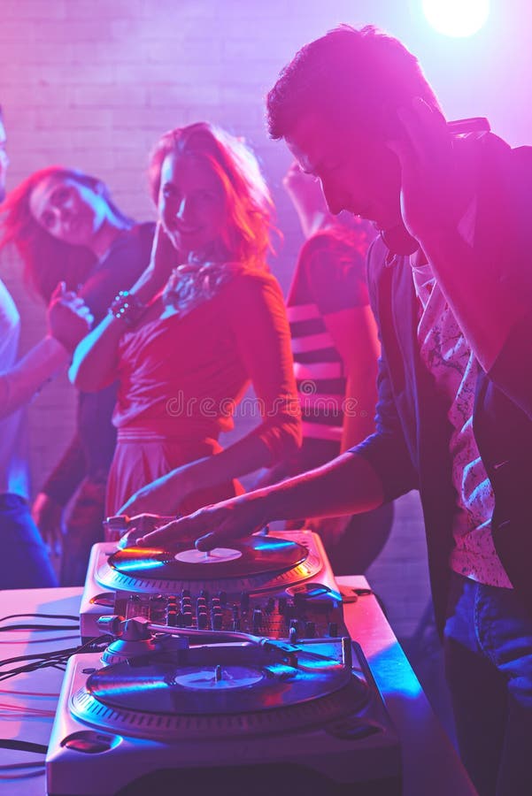 Male deejay adjusting sound on background of group of energetic dancers. Male deejay adjusting sound on background of group of energetic dancers