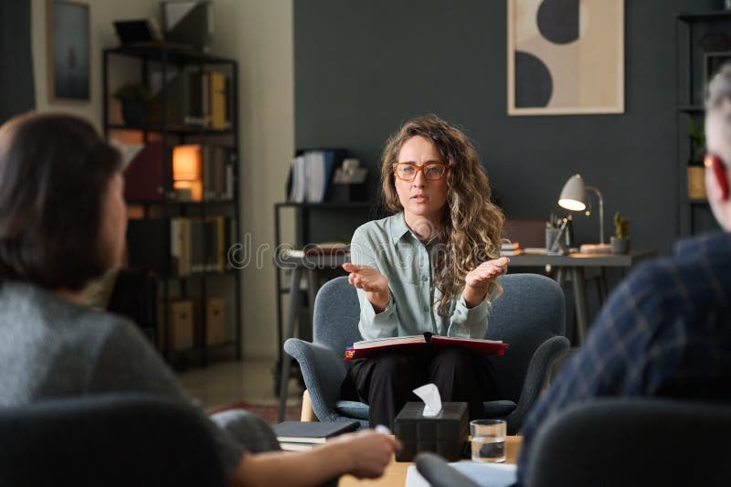 Discussing Work Strategies in Modern Office Environment. Three colleagues engaging in discussion about work strategies in a modern office setting, collaborating for project advancement and sharing ideas, seated around the table, Caucasian woman talking