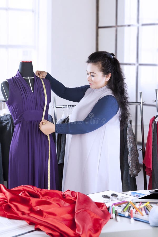 Diseñador de moda de sexo femenino que mide un vestido imagen de archivo Diseñador de moda de sexo femenino que mide un vestido imagen de archivo