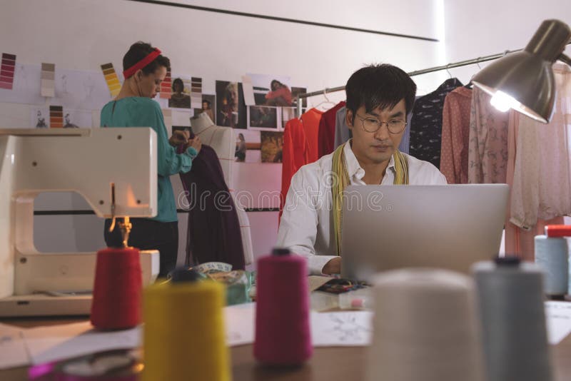 Diseñador de moda de sexo masculino que trabaja en el ordenador portátil mientras que maniquí femenino de la preparación del dise imagenes de archivo Diseñador de moda de sexo masculino que trabaja en el ordenador portátil mientras que maniquí femenino de la preparación del dise imagenes de archivo